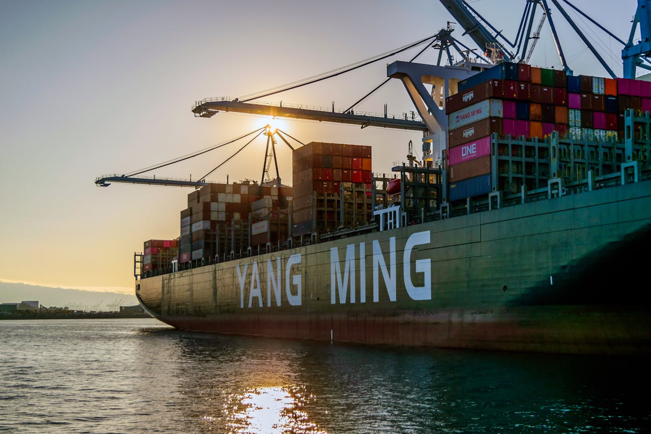 A large container ship with colorful cargo containers in a harbor during sunset, symbolizing global trade.